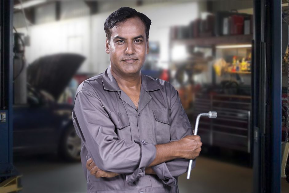 Friendly auto mechanic smiling next to a vehicle